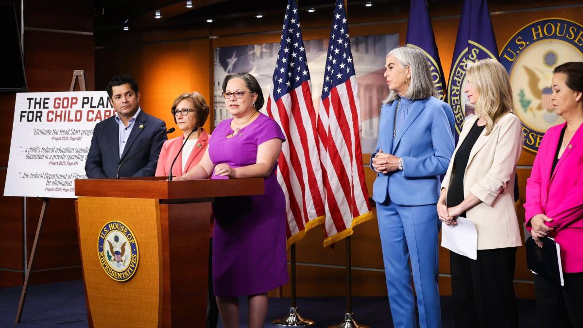 McClellan stands behind a podium flanked by Members of Congress, including Whip Katherine Clark, at a press conference on child care.