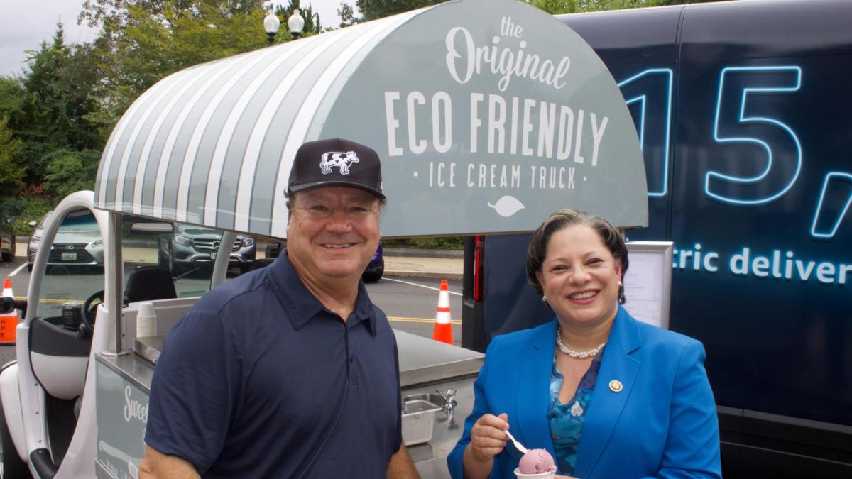 McClellan stands next to a man in front of an electric ice cream truck. 