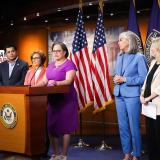 McClellan stands behind a podium flanked by Members of Congress, including Whip Katherine Clark, at a press conference on child care. 
