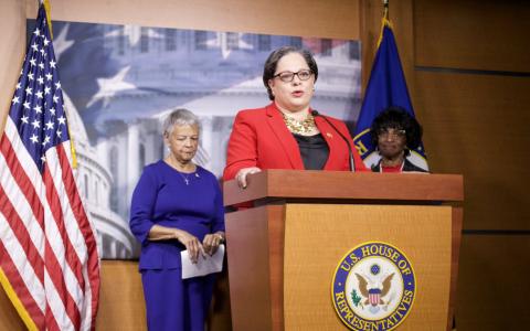 Rep. McClellan at a press conference, stands behind a podium speaking. 